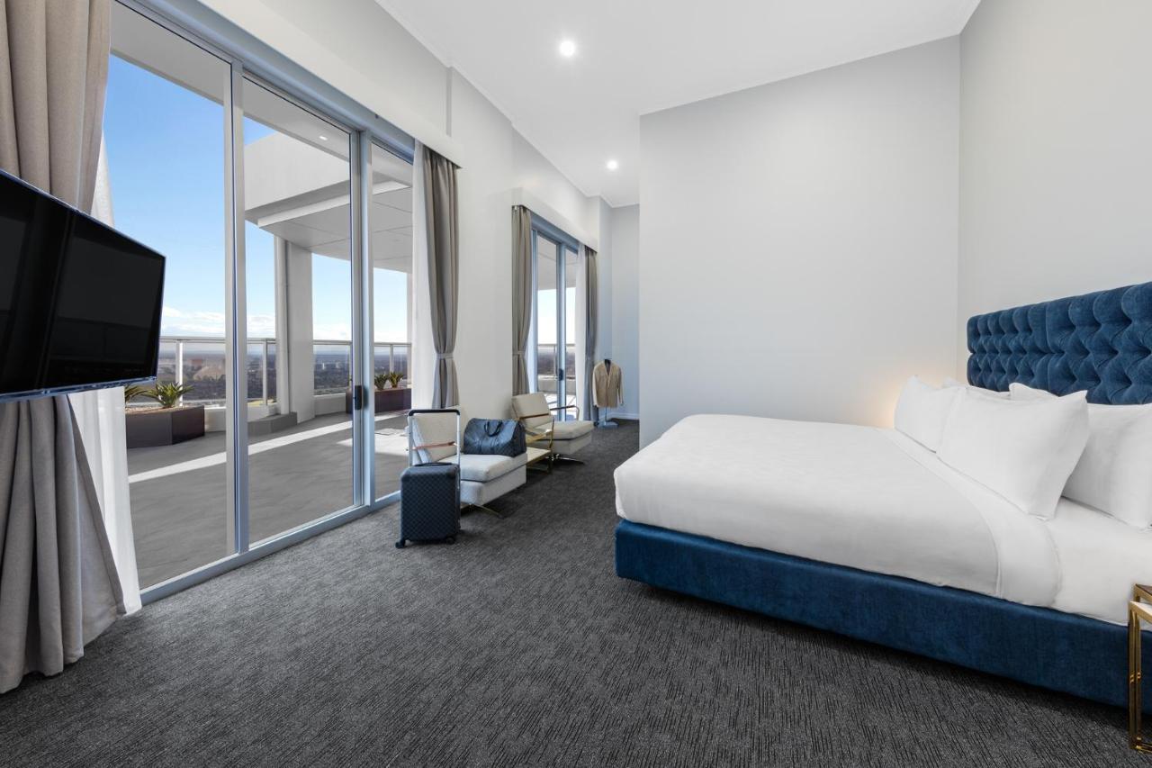 Meriton Suites Bondi Junction Сідней Екстер'єр фото The photo shows a modern and spacious hotel room. It features a large bed with a blue headboard, a flat-screen TV mounted on the wall, and a cozy seating area with a chair and small table. The room has large windows that offer natural light and a vie