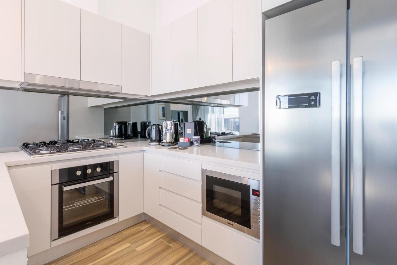 Meriton Suites Bondi Junction Сідней Екстер'єр фото The photo shows a modern kitchen with a clean and minimalist design. It features white cabinetry and a stainless steel refrigerator. The kitchen includes a gas stove with an oven below it, as well as a microwave. There are several kitchen appliances,