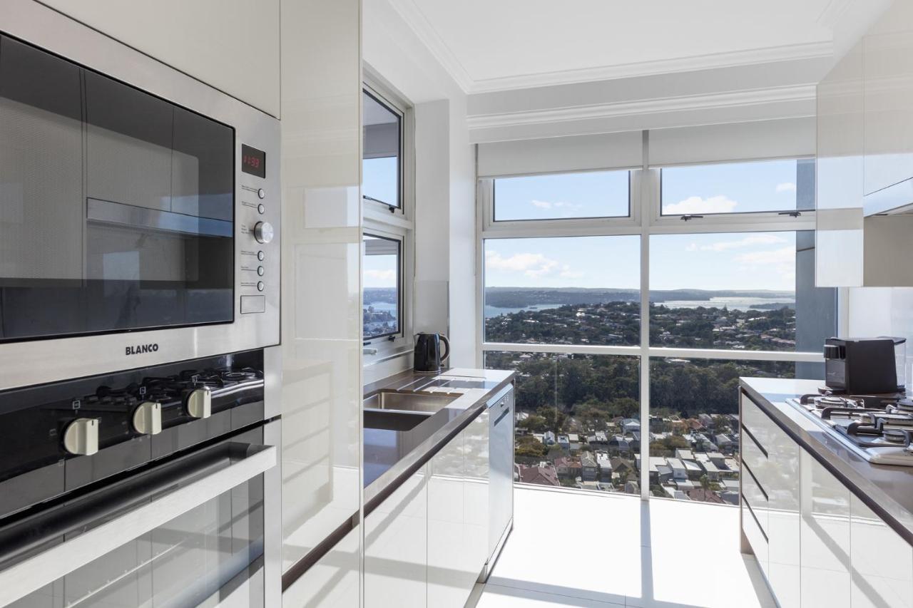 Meriton Suites Bondi Junction Сідней Екстер'єр фото The photo shows a modern kitchen with sleek, shiny white cabinets and a large window that offers a panoramic view of the outside landscape. The kitchen features built-in appliances, including an oven and a stove, with a stylish countertop. The spacio