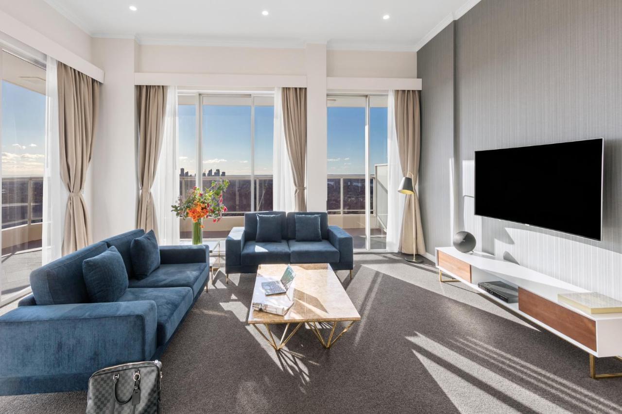 Meriton Suites Bondi Junction Сідней Екстер'єр фото The photo depicts a modern living room with a stylish and contemporary design. It features a cozy seating arrangement with a blue sofa and two matching armchairs. In front of the seating area is a coffee table with a geometric design. The room has la