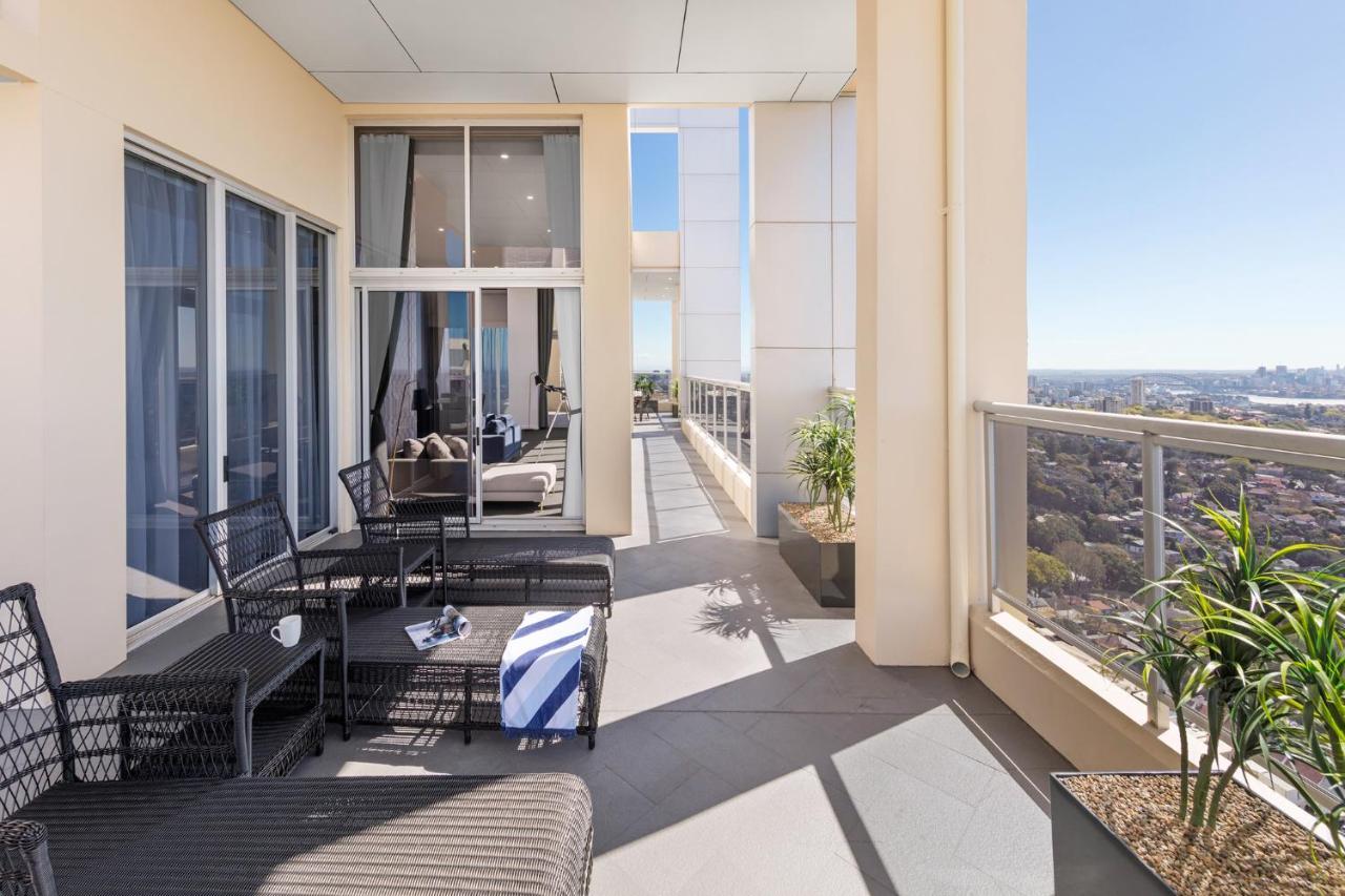 Meriton Suites Bondi Junction Сідней Екстер'єр фото The photo shows a spacious balcony or terrace area of a high-rise building. It features modern outdoor furniture, including a seating arrangement with dark wicker chairs and a table. There are cushions, and a blue and white striped blanket is draped 